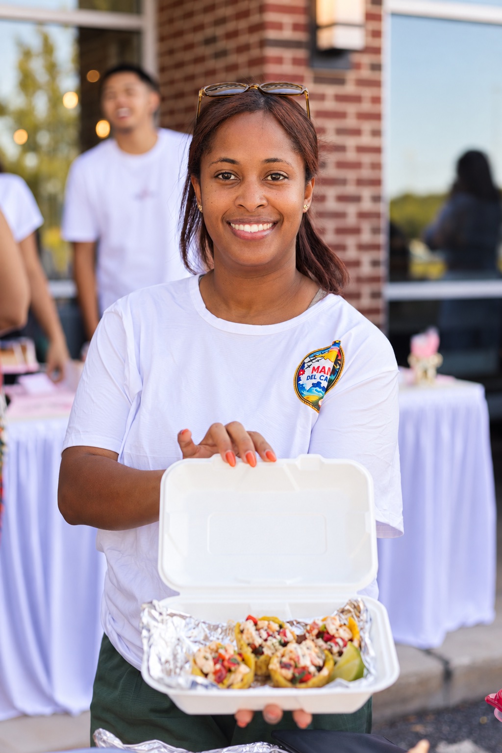 A smiling Mana del Caribe team member serving shrimp-filled plantain cups at an event